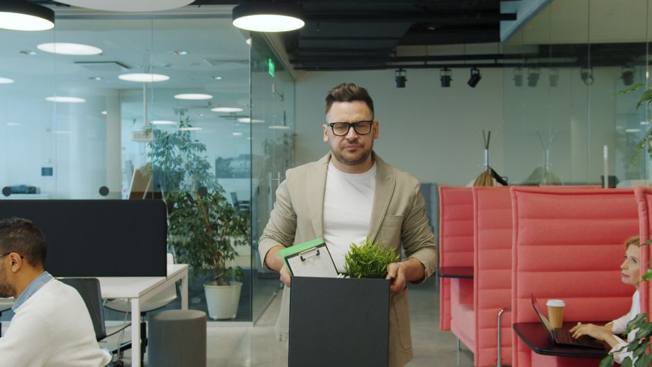Hombre con gafas saliendo de una oficina con una caja de pertenencias personales