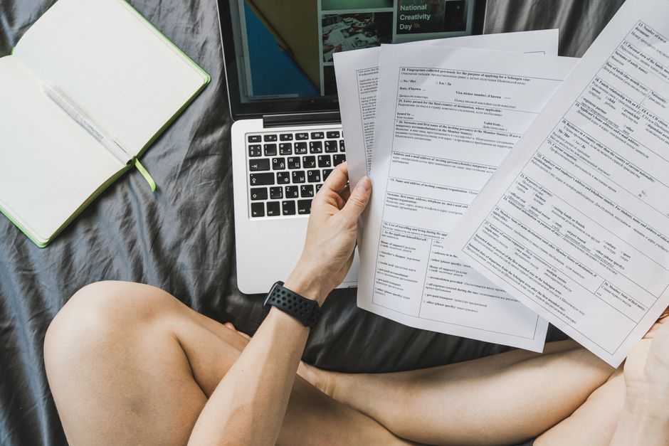 Persona sentada con un portátil repasando varios documentos impresos