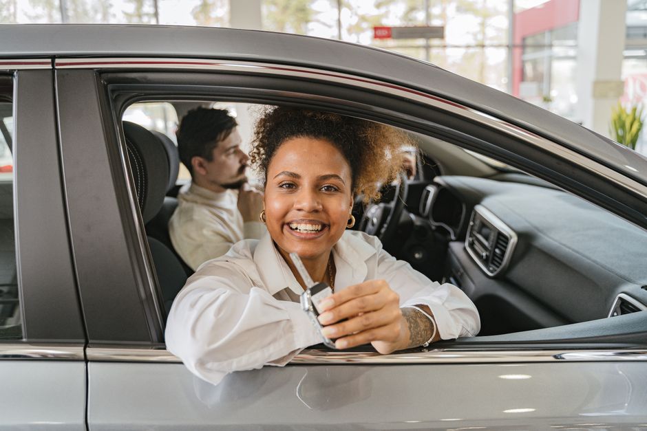 Compradora sentada al volante mostrando las llaves de un coche de segunda mano recién adquirido