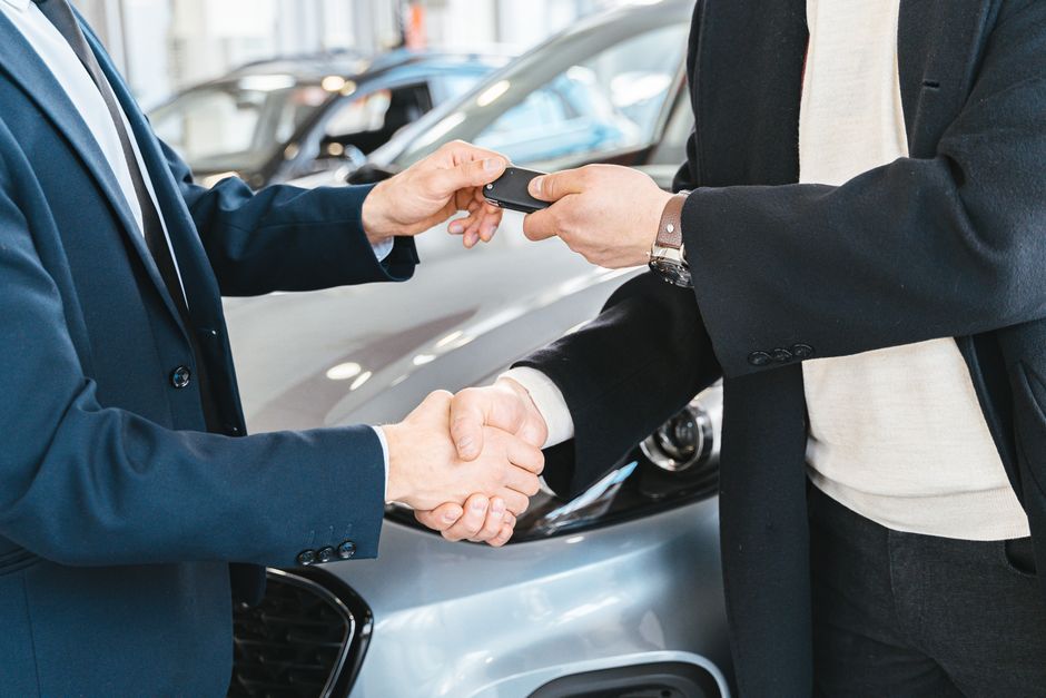 Vendedor y comprador cerrando con un apretón de manos la compraventa de un coche usado y entregando la llave