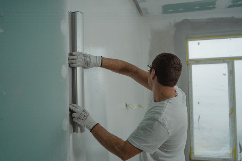 Albañil alisando con una regla la pared de un piso en obras durante una reforma de vivienda