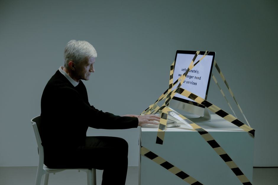 Hombre mayor sentado frente al ordenador leyendo su carta de despido en la oficina